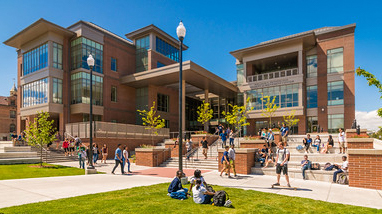 Exterior of the Pennington Student Achievement building, a modern, multi-story brick building with large bay windows, lightpoles lining walking paths, lawn areas and students passing in front of the building.