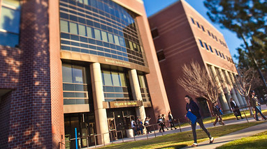 Exterior of the William J. Raggio Education building, a modern brick building with large windows, walkways and a lawn, with students walking in front of the building.