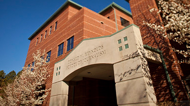 Exterior of the Reynolds School of Journalism, a modern brick building with "Reynolds School of Journalism" on the top of the the entrance.