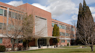 Exterior of the Scrugham Engineering and Mines building, an older brick building with large trees and grass areas in front of the building. 