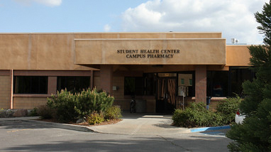 Exterior of the Student Health Center, a brick building with the building name  at the top of the entrance and a parking area next to the building.