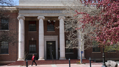 Exterior of Thompson Hall, an older brick building with large white columns in front of the entrance and large trees surrounding the front of the building.