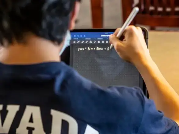 A student wearing a Nevada blue shirt uses an Apple pencil to do math homework on an iPad.